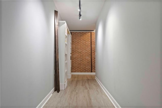 hallway with light wood-type flooring, track lighting, and brick wall