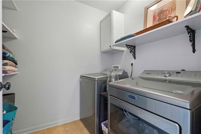 clothes washing area with cabinets, light tile patterned floors, and washing machine and clothes dryer