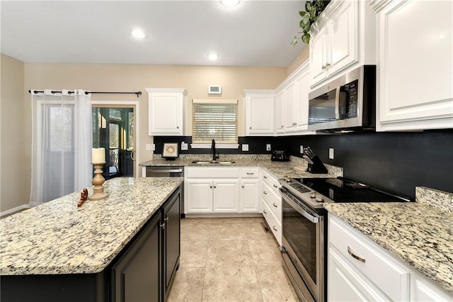 kitchen with light stone countertops, a kitchen island, white cabinetry, stainless steel appliances, and sink