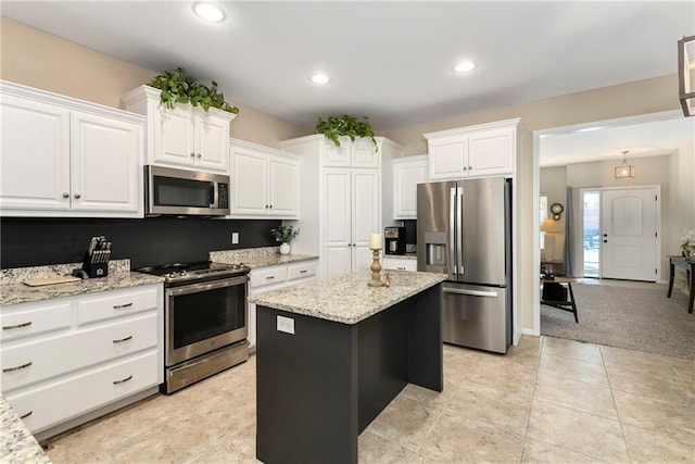 kitchen featuring light stone countertops, appliances with stainless steel finishes, a center island, white cabinetry, and light colored carpet