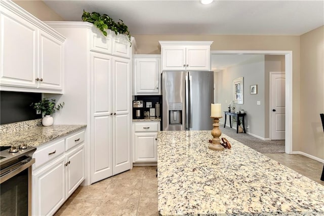 kitchen featuring light tile patterned floors, light stone countertops, white cabinetry, and appliances with stainless steel finishes