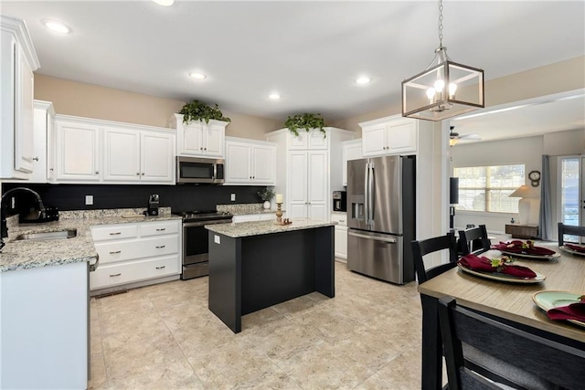 kitchen featuring appliances with stainless steel finishes, a center island, white cabinetry, sink, and hanging light fixtures