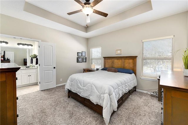 bedroom featuring ensuite bathroom, light colored carpet, ceiling fan, and a tray ceiling