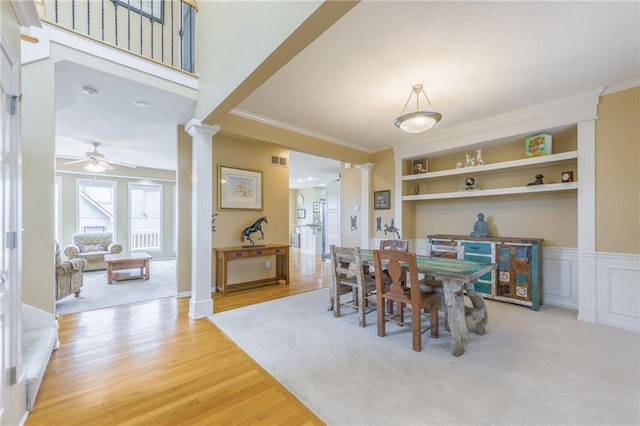 dining area with ornate columns, built in features, wood-type flooring, ceiling fan, and crown molding