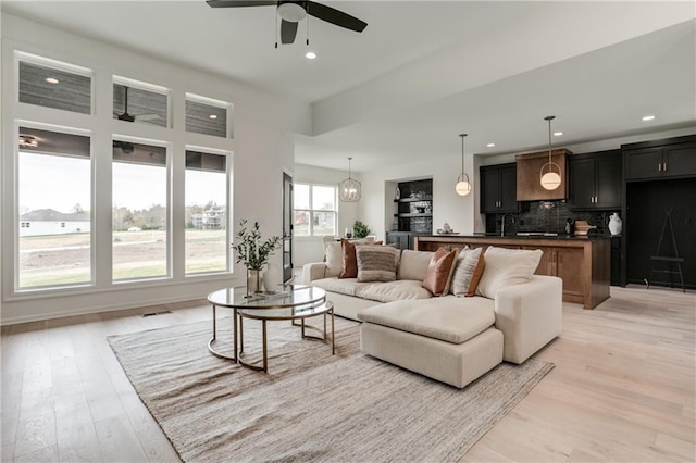 living room with ceiling fan with notable chandelier, light hardwood / wood-style floors, and sink