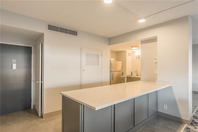 kitchen featuring gray cabinets, sink, kitchen peninsula, and stainless steel refrigerator