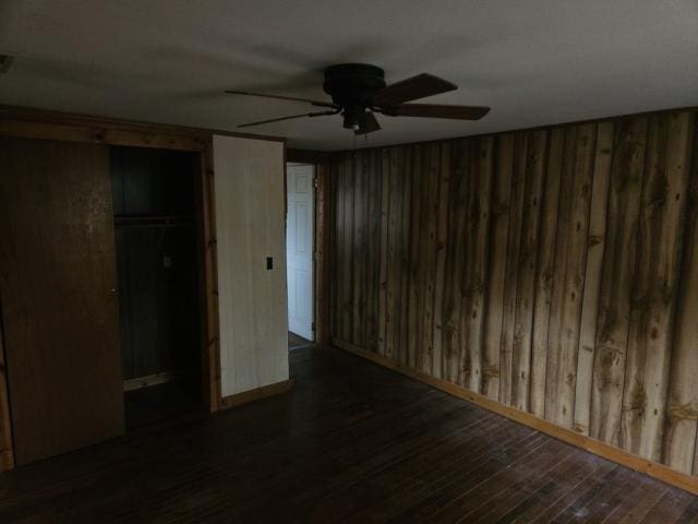 unfurnished bedroom with ceiling fan, wood walls, dark wood-type flooring, and a closet