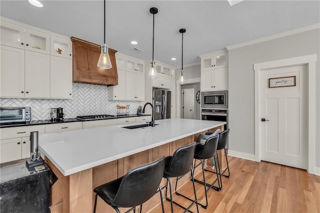 kitchen featuring white cabinets, a center island with sink, sink, decorative backsplash, and stainless steel appliances