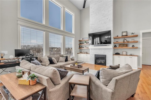 living room featuring a stone fireplace, a towering ceiling, and light hardwood / wood-style flooring