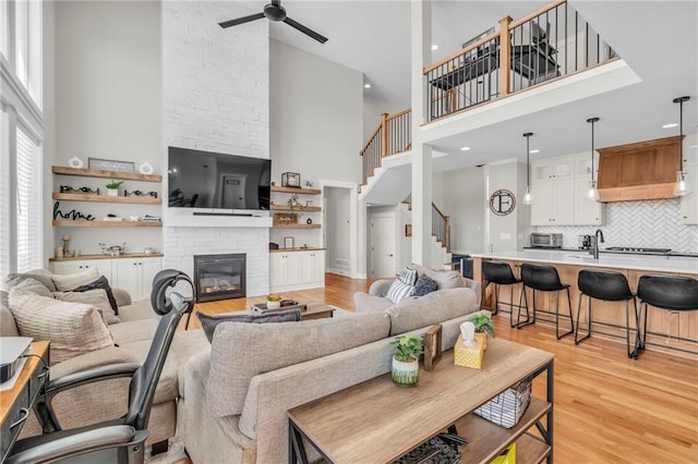 living room with a stone fireplace, ceiling fan, a high ceiling, and light wood-type flooring