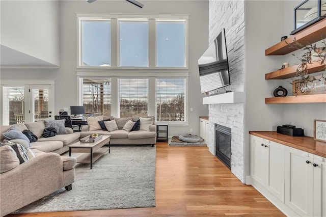 living room featuring ceiling fan, a stone fireplace, a high ceiling, and light hardwood / wood-style flooring