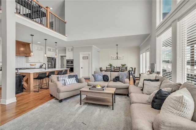 living room featuring ornamental molding, light wood-type flooring, a high ceiling, and an inviting chandelier