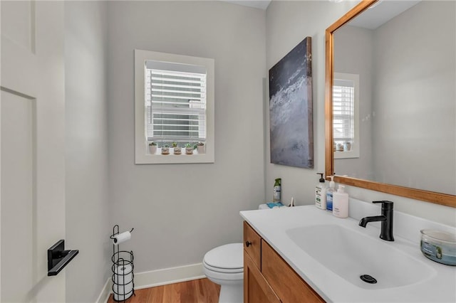 half bath featuring baseboards, vanity, toilet, and wood finished floors