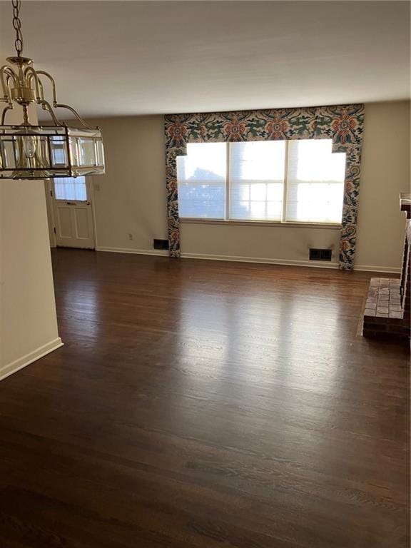 empty room featuring a notable chandelier, dark hardwood / wood-style floors, and a brick fireplace