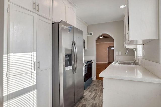 kitchen featuring sink, black electric range oven, stainless steel refrigerator with ice dispenser, white cabinets, and light wood-type flooring