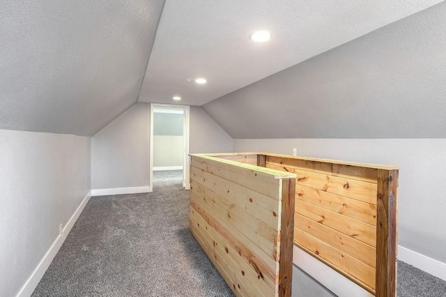 additional living space with dark colored carpet, a textured ceiling, and vaulted ceiling