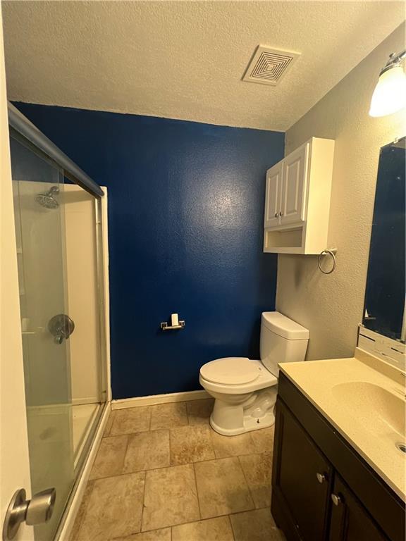 bathroom with a shower with door, vanity, a textured ceiling, and toilet