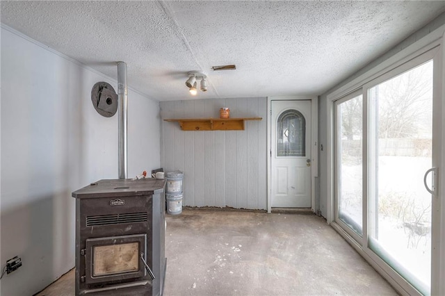 interior space with a wood stove, a textured ceiling, and wooden walls