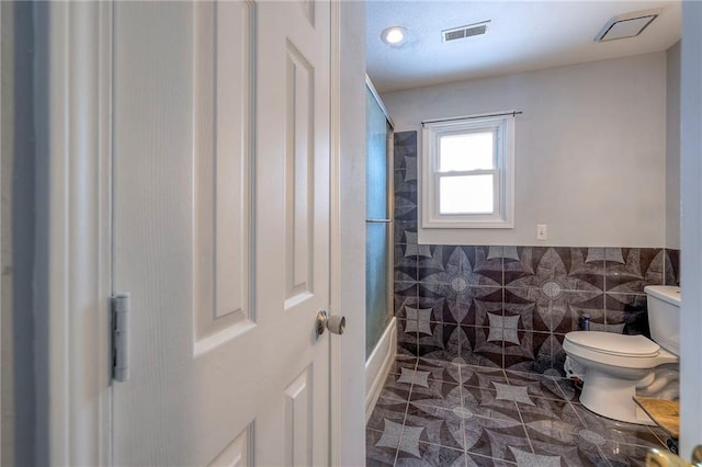 bathroom with an enclosed shower, toilet, tile walls, and tile patterned floors