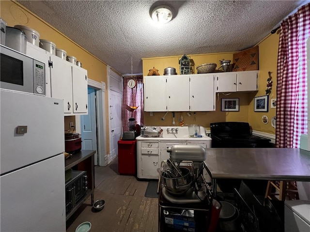 kitchen featuring black gas range oven, a textured ceiling, dark wood-type flooring, white refrigerator, and white cabinetry