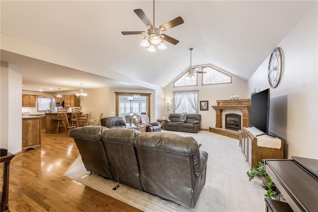 living room featuring ceiling fan with notable chandelier, light hardwood / wood-style flooring, and vaulted ceiling