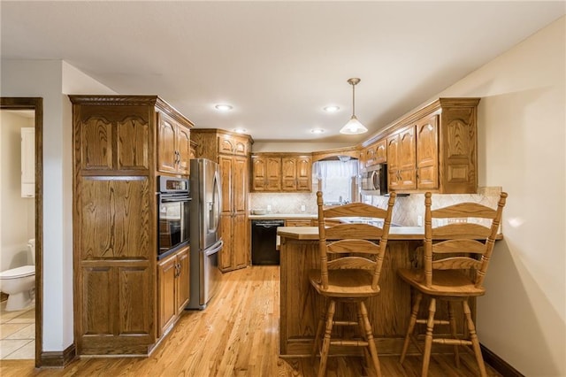 kitchen with pendant lighting, a breakfast bar area, light wood-type flooring, tasteful backsplash, and stainless steel appliances