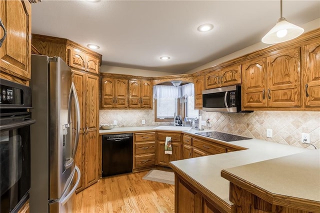 kitchen featuring sink, hanging light fixtures, kitchen peninsula, black appliances, and light wood-type flooring