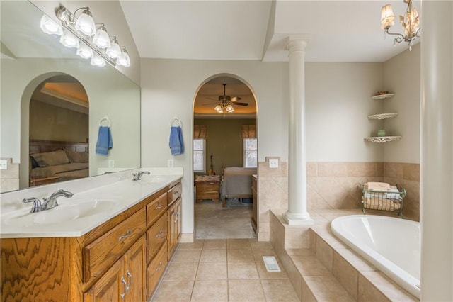 bathroom with tile patterned flooring, a relaxing tiled tub, decorative columns, vanity, and ceiling fan with notable chandelier