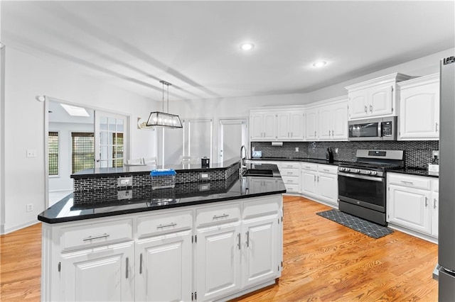 kitchen with appliances with stainless steel finishes, sink, white cabinets, a center island, and hanging light fixtures