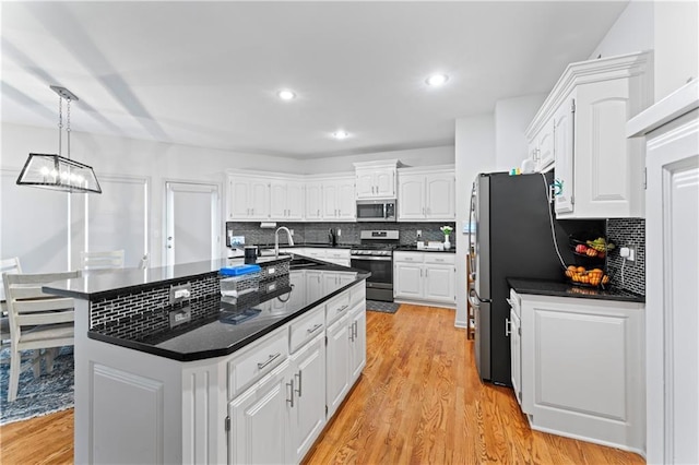 kitchen with stainless steel appliances, a kitchen island with sink, pendant lighting, light hardwood / wood-style flooring, and white cabinets