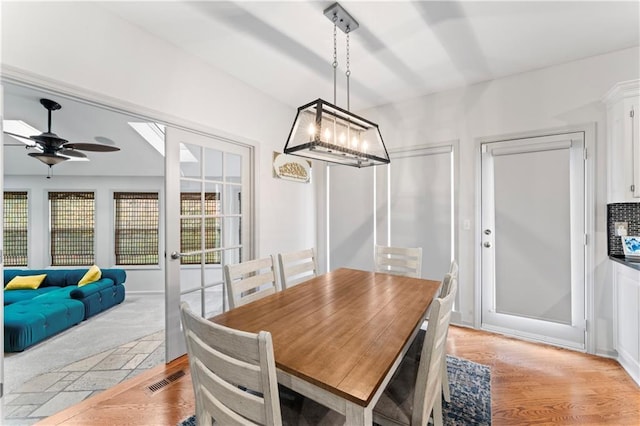 dining space with ceiling fan with notable chandelier and light hardwood / wood-style flooring