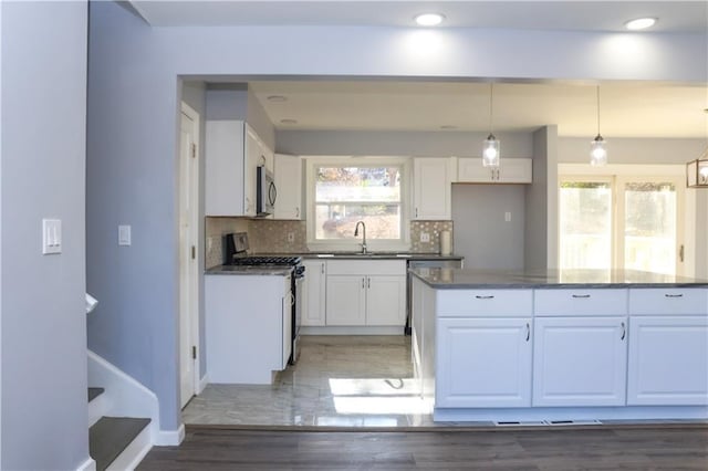 kitchen with backsplash, gas range gas stove, sink, decorative light fixtures, and white cabinetry