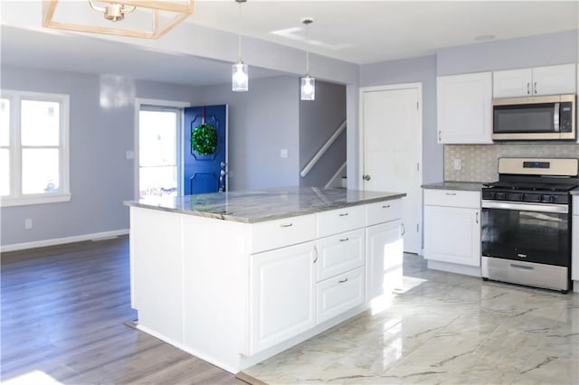 kitchen featuring backsplash, white cabinets, light stone countertops, appliances with stainless steel finishes, and a kitchen island