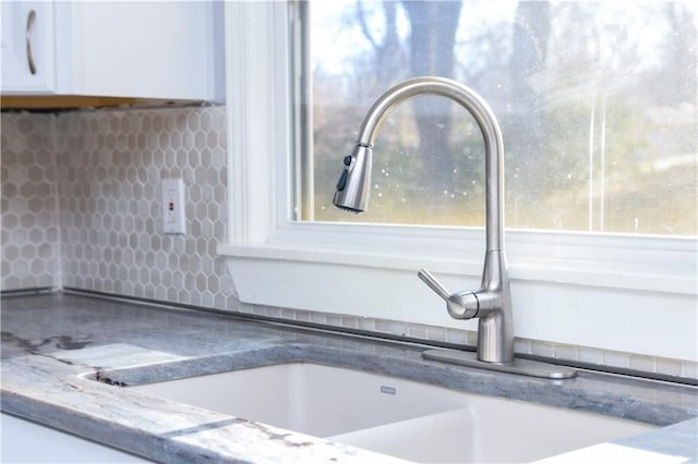 details featuring tasteful backsplash, white cabinetry, and sink