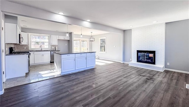 kitchen with a brick fireplace, tasteful backsplash, dark hardwood / wood-style flooring, white cabinets, and appliances with stainless steel finishes