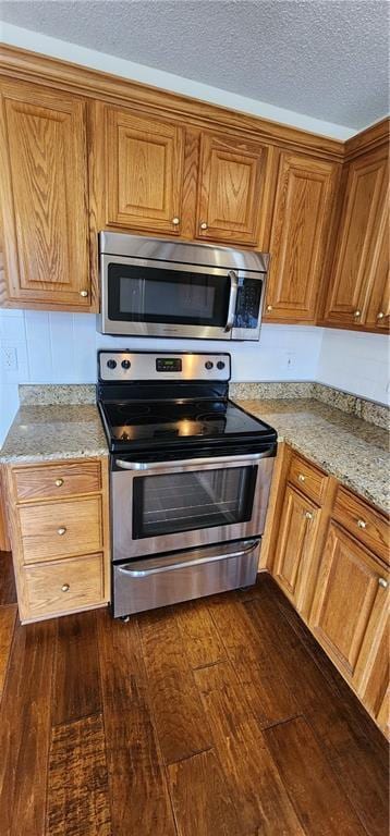 kitchen with a textured ceiling, light stone countertops, stainless steel appliances, and dark hardwood / wood-style floors