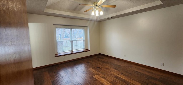 empty room featuring ceiling fan, dark wood-type flooring, and a tray ceiling