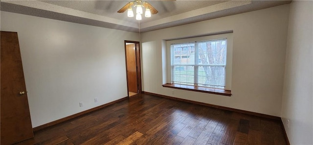 empty room with a raised ceiling, ceiling fan, and dark hardwood / wood-style flooring