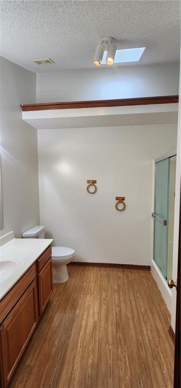 bathroom featuring a skylight, wood-type flooring, a textured ceiling, vanity, and a shower with shower door