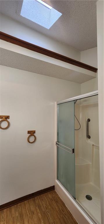 bathroom featuring hardwood / wood-style floors, a shower with door, a textured ceiling, and a skylight