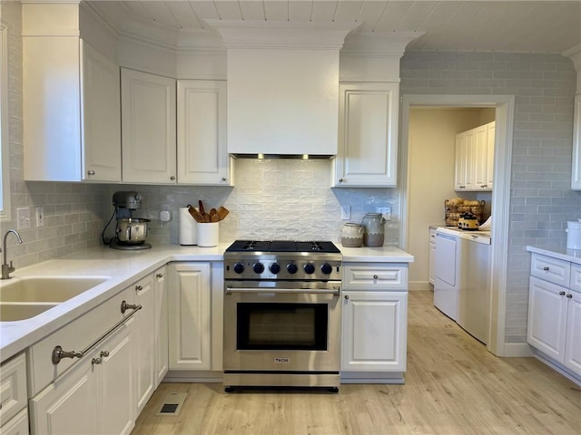 kitchen with decorative backsplash, white cabinetry, high end stove, and light hardwood / wood-style flooring