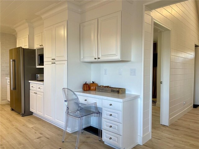 kitchen with white cabinets, ornamental molding, stainless steel appliances, and light hardwood / wood-style flooring