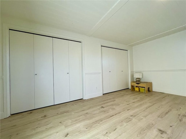 unfurnished bedroom with light wood-type flooring and multiple closets