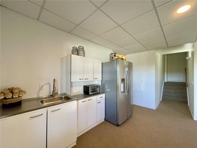 kitchen with stainless steel fridge, sink, white cabinets, and light carpet