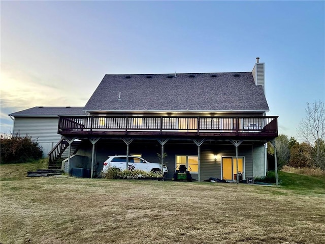 back house at dusk featuring a lawn and a deck