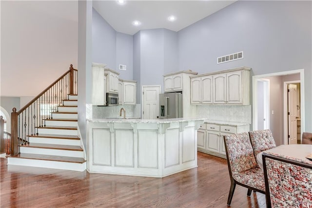 6764 Longview Rd, Shawnee, KS 66218 - kitchen with appliances with stainless steel finishes, a towering ceiling, a peninsula, wood finished floors, and a kitchen bar