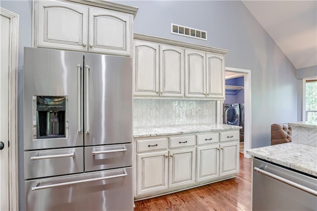 6764 Longview Rd, Shawnee, KS 66218 - kitchen featuring appliances with stainless steel finishes, vaulted ceiling, light wood-style flooring, separate washer and dryer, and decorative backsplash