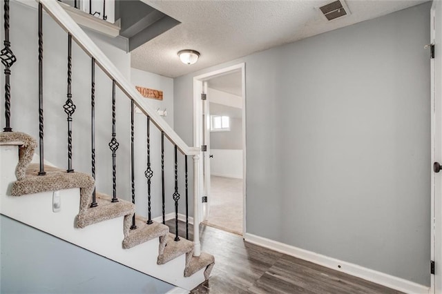 stairs with baseboards, visible vents, a textured ceiling, and wood finished floors