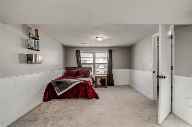 bedroom featuring a wainscoted wall, a textured ceiling, and light colored carpet