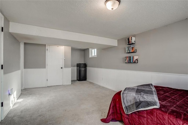 carpeted bedroom featuring a wainscoted wall and a textured ceiling